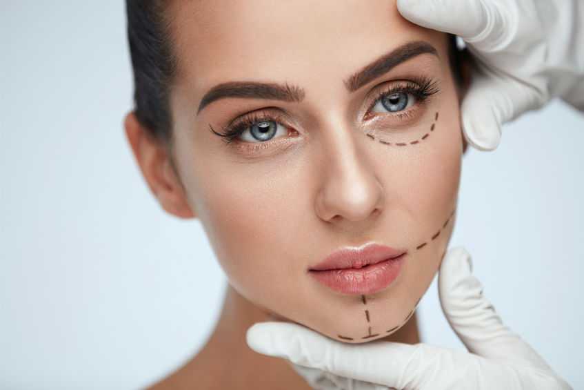 Facial Beauty Treatment. Beautiful Young Female With Smooth Skin, Perfect Makeup And Surgical Lines. Closeup Of Beautician Hands Touching Woman Face Before Plastic Surgery Operation. High Resolution