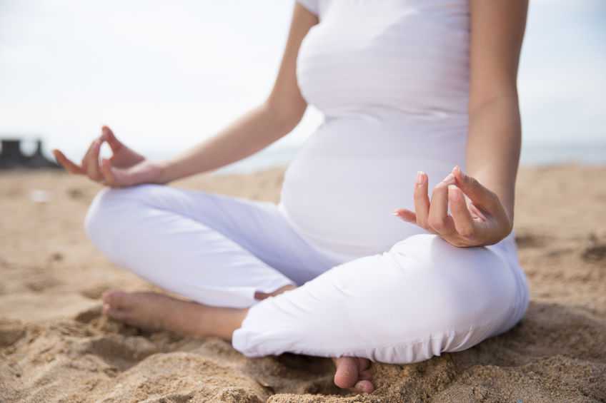 close up of pregnant woman doing yoga in the beach